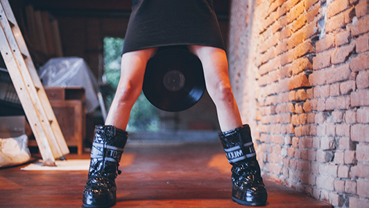 Girl in black dress and boots holding a vinyl between her legs