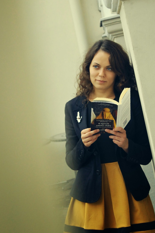 Girl leaned against a wall while holding a book.