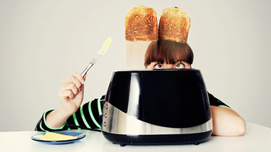 woman holding butter knife watching toast jump out of toaster