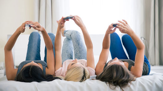 three woman lying on bed playing games on phone