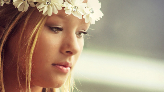 Girl with flowers in her hair looking down.