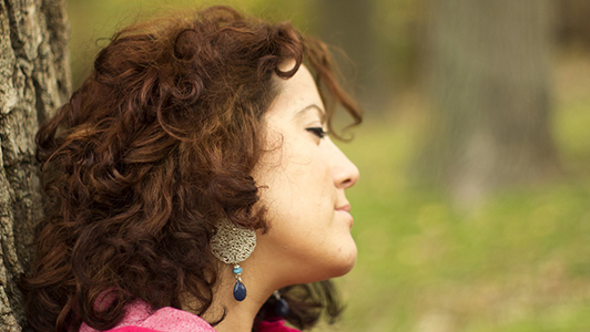 Brunette with curly hair leaned on a tree.