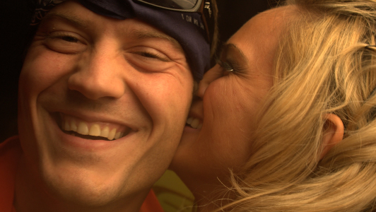 Blonde girl kissing a smiling guy on the cheek.