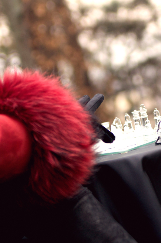 Arm in red coat with leather glove moving a chess piece.