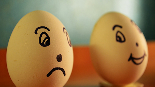 Two eggs: one with sad and one with happy face drawn on it.