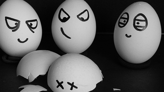 Three eggs with mean-looking faces standing over a broken egg shell.