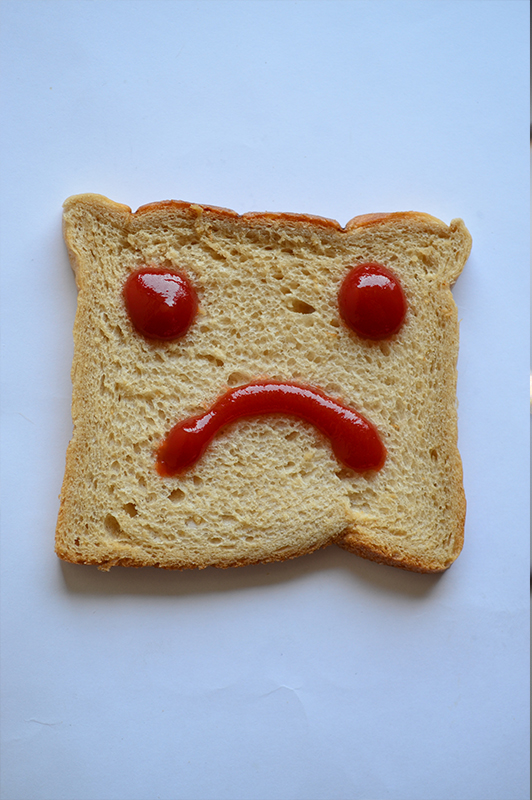 A piece of toast with a sad face made of ketchup