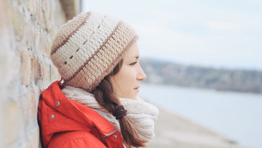 woman standing outside alone against wall overlooking ocean on beach