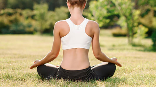 back of woman practicing yoga in grass