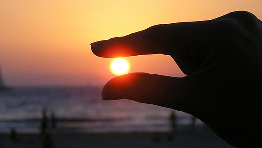 Girl holding her fingers so that it looks like she's holding Sun setting.