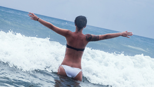 Girl in a black and white bikini holding her arms spread while standing in water.