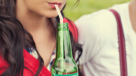 Girl drinking from a bottle and a guy is sitting next to her.