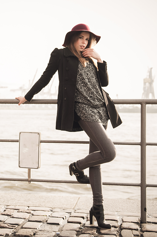 Girl in high heels wearing a hat while leaning on a fance.