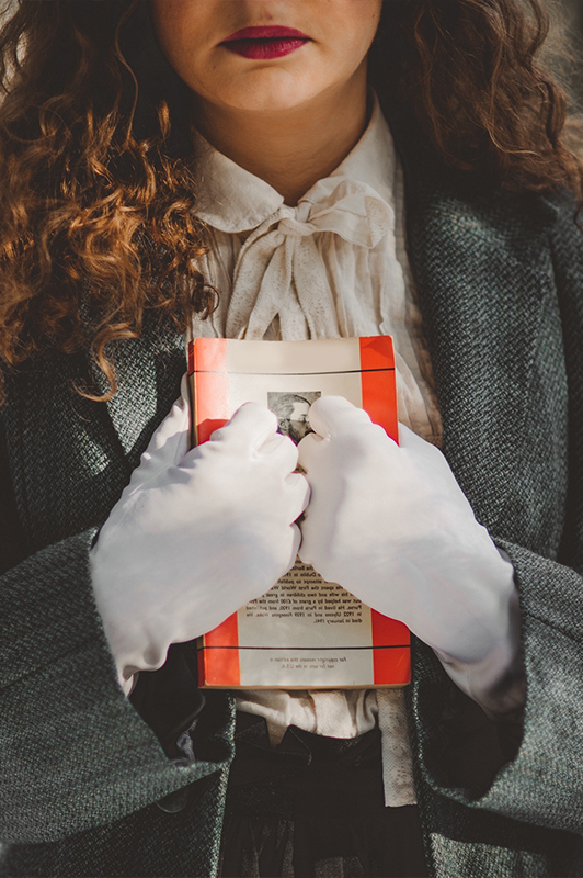 A woman with white gloves holding a book against her chest.