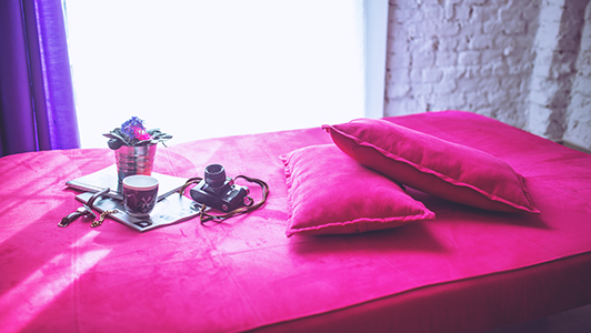 Pink bed with pillows, flowers, mug and camera on it.