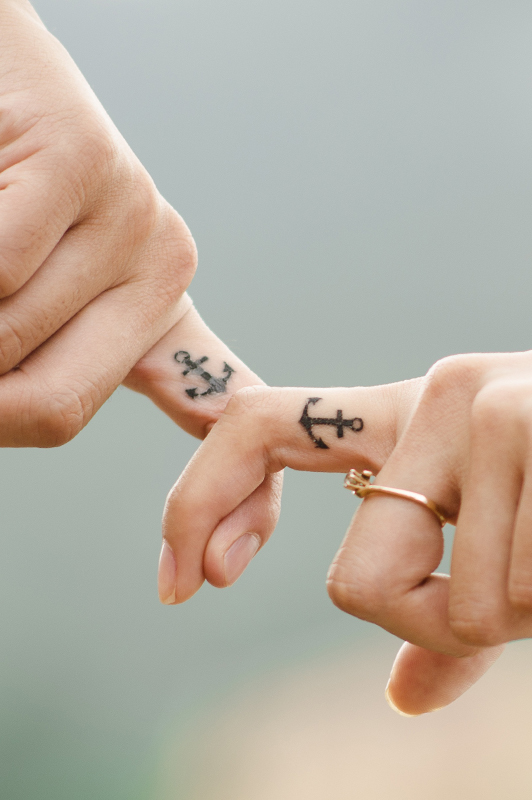 Couple holding hands with matching anchor tattoos on their fingers.