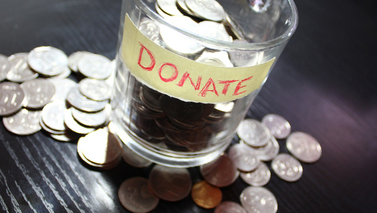 A glass on which says donate filled with coins