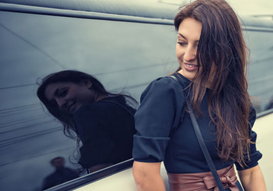 young woman leaning on car looking at reflection of guy approaching