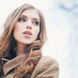 view of woman wearing trenchcoat with curly hair and cloudy sky