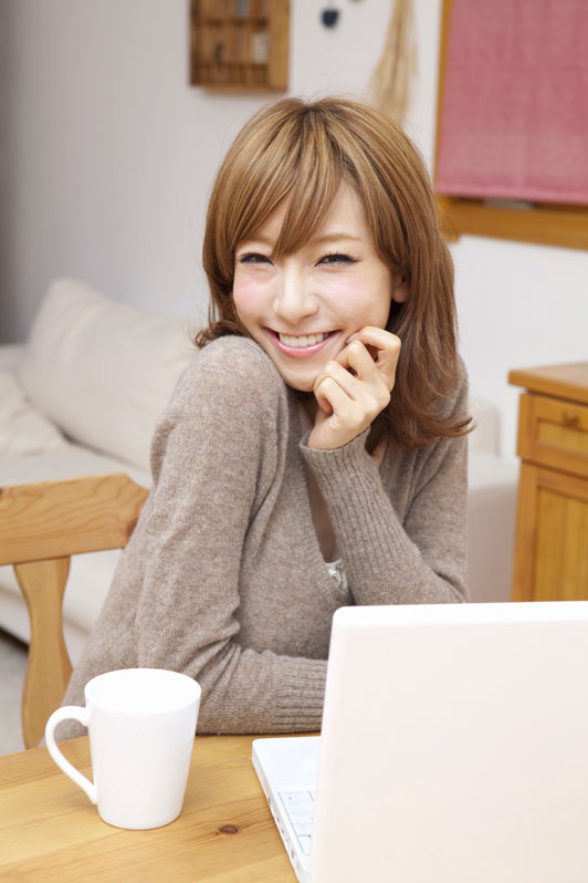 girl in front of laptop smiling with warm beverage