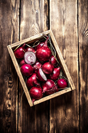 box of red onions on wooden table