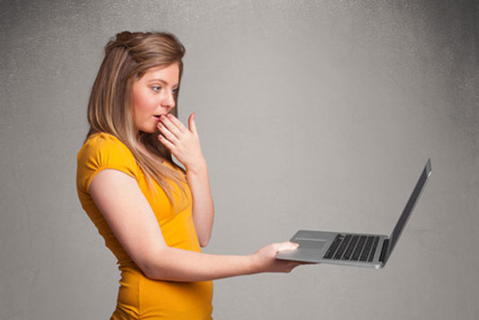 surprised young woman in yellow shirt holding laptop with one hand