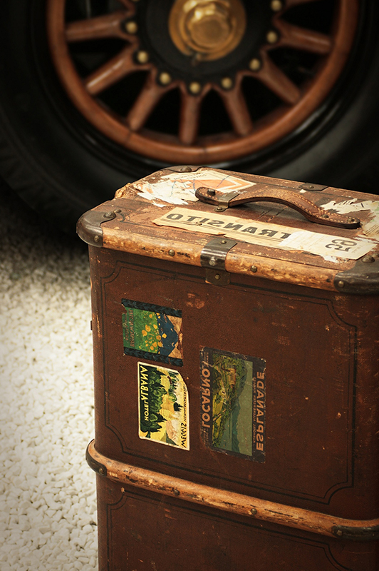 An old luggage with postcards stuck to it, and a tire in the background