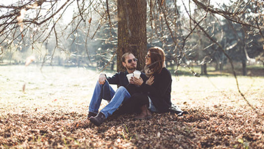 two people sitting under tree holding cups