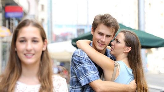 unfaithful man checking out another woman while being hugged by his girlfriend