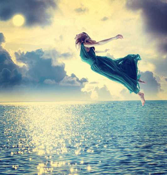 woman in blue dress flying into sunset over ocean