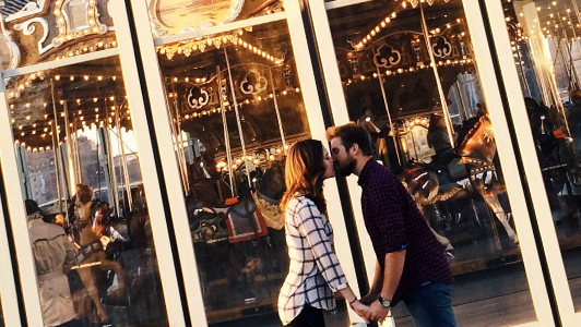 couple kissing in front of a merry-go-round