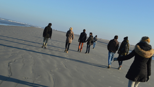 Girl in a jacket walking behind a group of people on a beach.