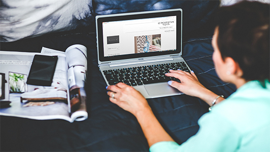 Girl lying on a bed and browsing on her laptop.