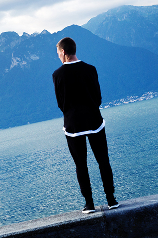 Guy standing on the edge of a wall looking at a lake.