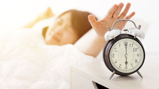 girl waking up reaching for alarm clock