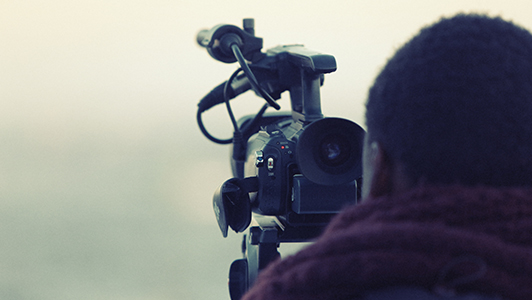 A guy with a scarf looking through a camera.