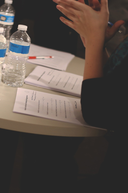 Girl sitting at a table with papers and water bottles in front of her.