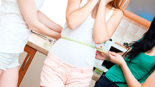 midsection of girl being measured by two other girls