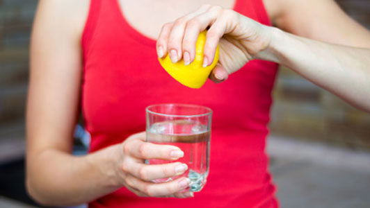 woman in red tank top squeezing lemon into water