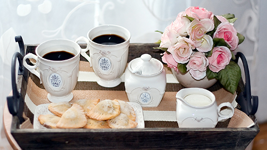 Two cups of coffe, sugar bowl, cookies, and flowers on a platter.