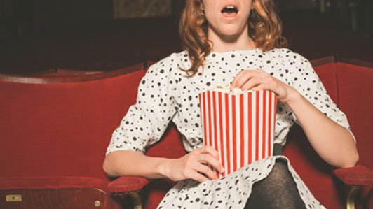 young woman in theater watching moving eating popcorn