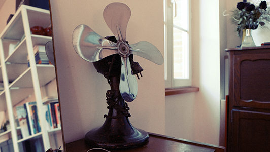 A vintage fan standing near a mirror.