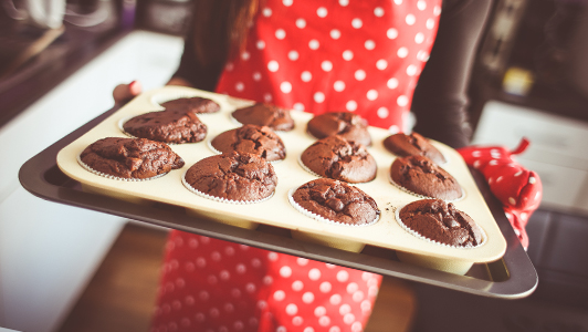 Girl with red polka dot apron holding a trey of muffins.