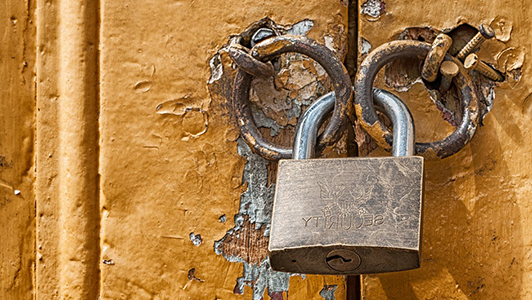 Padlock on the old door with damaged yellowish paint.