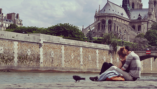 A couple sitting near the river in Paris, a black raven next to them.