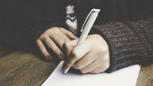 woman in grey sweater taking notes with white pen
