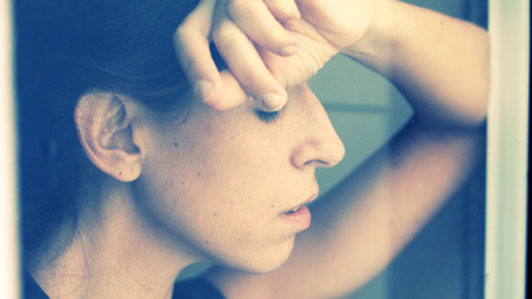 woman in front of window with back of hand on forehead