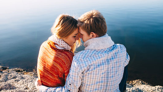 couple sitting close before lake