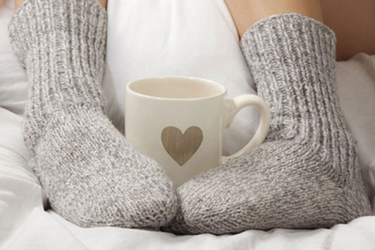 woman in grey socks hugging coffee cup with feet