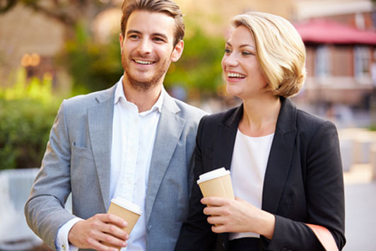 couple dressed up in suits walking down street holding coffee cups